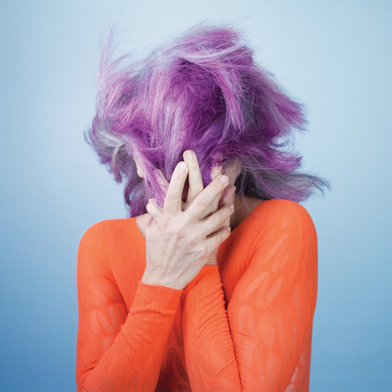 Atrás do cabelo entre o grisalho e o lilás, Tetê esconde e mostra o rosto moldado em "Outro Lugar"
