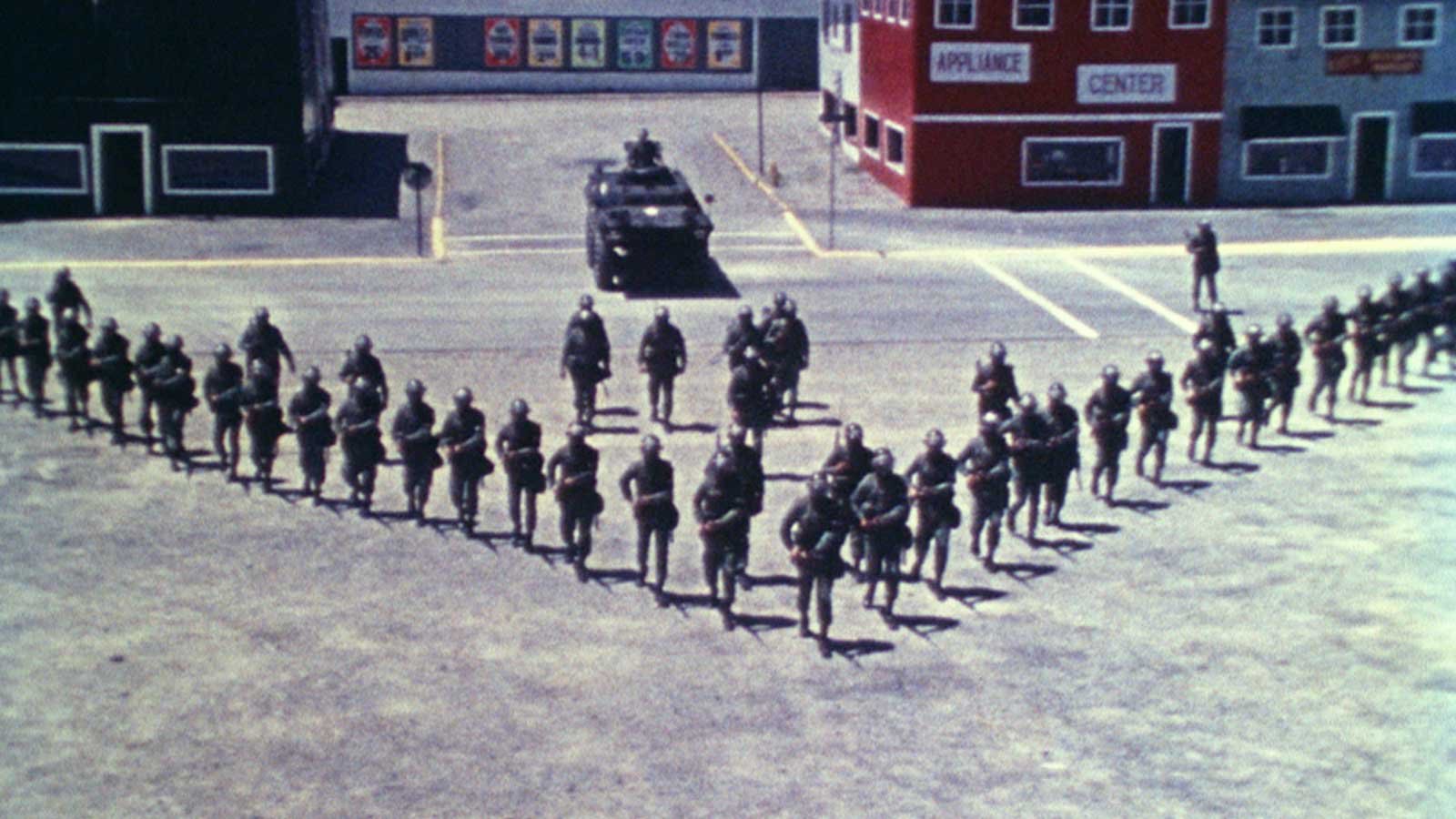 Militares reais se postam diante da cidade fictícia de Riotsville