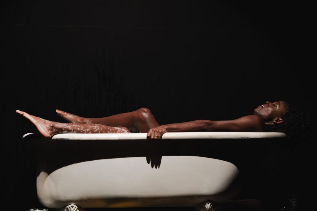 Na imagem, a atriz negra trans Aretha Sadick interpeta Lady Macbeth, e está dentro de uma banheira.
